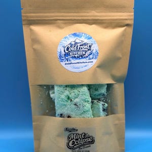 May include: A brown paper bag with a clear window displaying mint ice cream. The ice cream is light green with dark chocolate chips. The bag has a sticker that says "Cold Front Kitchen" and another that says "Cosmic Creamery Mint Eclipse Ice Cream".