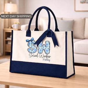 May include: A canvas tote bag with navy blue accents and handles. The bag features the initials "SW" in a floral design, the words "Social Worker" and a name. A navy blue ribbon is tied to the handles.