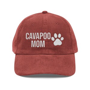 May include: A red corduroy baseball cap with the text "CAVAPOO MOM" in white block letters and a white paw print. The cap has a curved brim and an adjustable strap.
