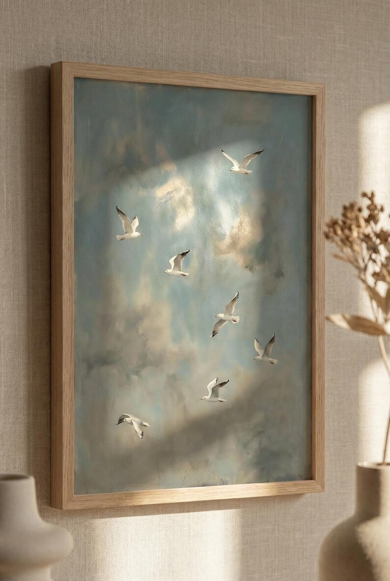 May include: A framed artwork featuring a flock of seagulls in flight against a cloudy sky. The painting has a soft, muted color palette of blues, whites, and browns. The wooden frame adds a natural touch to the artwork.
