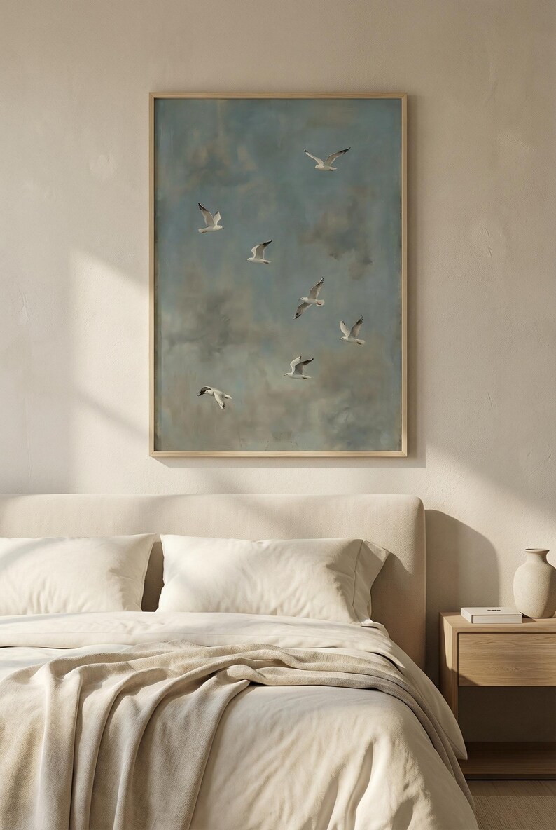 May include: A framed artwork featuring a flock of seagulls soaring against a cloudy, blue sky. The painting has a muted color palette with a wooden frame. The artwork is displayed above a bed with cream-colored bedding and a wooden nightstand.