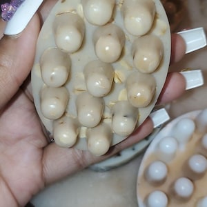May include: Oval massage tool featuring numerous rounded, pale nodules. The tool is beige with visible grains, and the nodules are a lighter shade. Another similar tool is visible in the background.