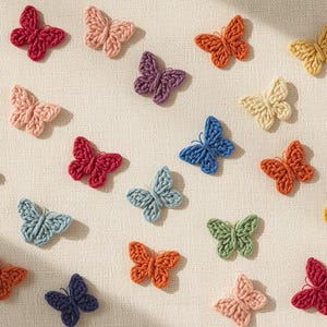 May include: A collection of colorful, crocheted butterfly appliques in various shades of pink, orange, red, purple, blue, green, and yellow. The butterflies are arranged on a cream-colored surface, creating a visually appealing pattern.
