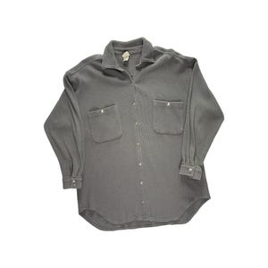 May include: A grey long-sleeved shirt with two front pockets and a button-down closure. The shirt features a collared neckline and buttoned cuffs. The fabric appears to be a soft, textured material.