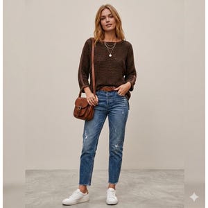 May include: A woman wearing a brown knit sweater, blue jeans, and white sneakers. She is carrying a brown leather crossbody bag. The jeans have distressed details. The sweater has a textured pattern.