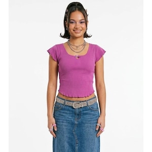 May include: A magenta ribbed knit top with a square neckline and frilled edges. The top has short sleeves and a small bow detail at the neckline. The person is wearing a denim skirt and a silver belt.