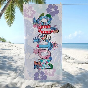 May include: A beach towel with the word "Lilo & Stitch" in colourful letters, with the characters integrated into the design. The towel has a light blue background with floral and leaf patterns, and is hanging on a clothesline on a sunny beach.