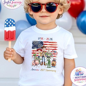 K&ouml;nnte beinhalten: Ein Kind mit roter Sonnenbrille und einem wei&szlig;en T-Shirt mit einer Grafik der amerikanischen Flagge und Zeichentrickfiguren. Das Shirt zeigt den Text "1776-2026" und "America - 250th Anniversary". Das Kind h&auml;lt ein rot-wei&szlig;-blaues Eis.