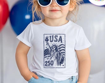 May include: A child wearing a white t-shirt with a USA graphic featuring the Statue of Liberty and the number 250. The child is also wearing a patriotic bow, round white sunglasses, and blue jeans. Red, white, and blue balloons are in the background.