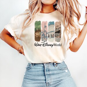 Puede incluir: Camiseta color crema con un gr&aacute;fico colorido de los lugares emblem&aacute;ticos de Walt Disney World. El dise&ntilde;o incluye im&aacute;genes de un castillo, una escena del parque y otras atracciones, con las palabras "Walt Disney World" en escritura negra.