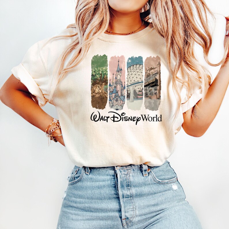 Puede incluir: Camiseta color crema con un gr&aacute;fico colorido de los lugares emblem&aacute;ticos de Walt Disney World. El dise&ntilde;o incluye im&aacute;genes de un castillo, una escena del parque y otras atracciones, con las palabras "Walt Disney World" en escritura negra.