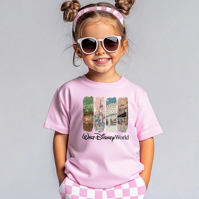 Puede incluir: Una camiseta rosa con un gr&aacute;fico de "Walt Disney World". El gr&aacute;fico presenta cuatro im&aacute;genes rectangulares verticales con escenas de parques de Disney. La ni&ntilde;a lleva gafas de sol y una diadema rosa y blanca.