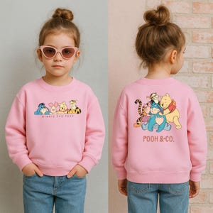 May include: A pink sweatshirt featuring Winnie the Pooh characters on the front and back. The front displays Eeyore, Piglet, Pooh, and Tigger with the text "Winnie the Pooh." The back shows the characters hugging with "Pooh & Co." text.