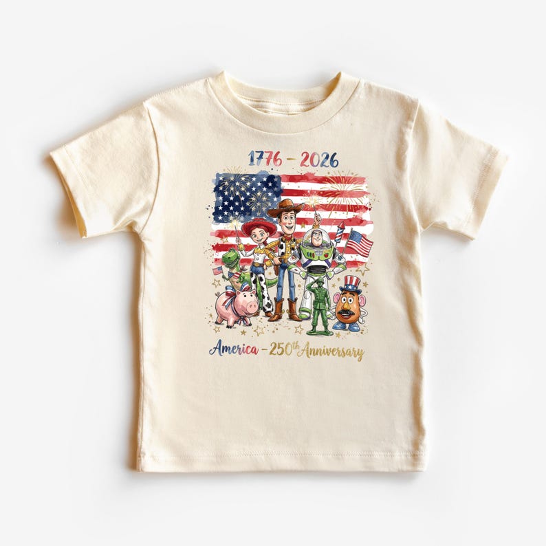 K&ouml;nnte beinhalten: Cremefarbenes T-Shirt mit einer Grafik von Zeichentrickfiguren vor einer amerikanischen Flagge. Der Text "1776-2026" und "America - 250th Anniversary" sind ebenfalls abgebildet. Das Design ist in Rot, Wei&szlig;, Blau und Gold gehalten.