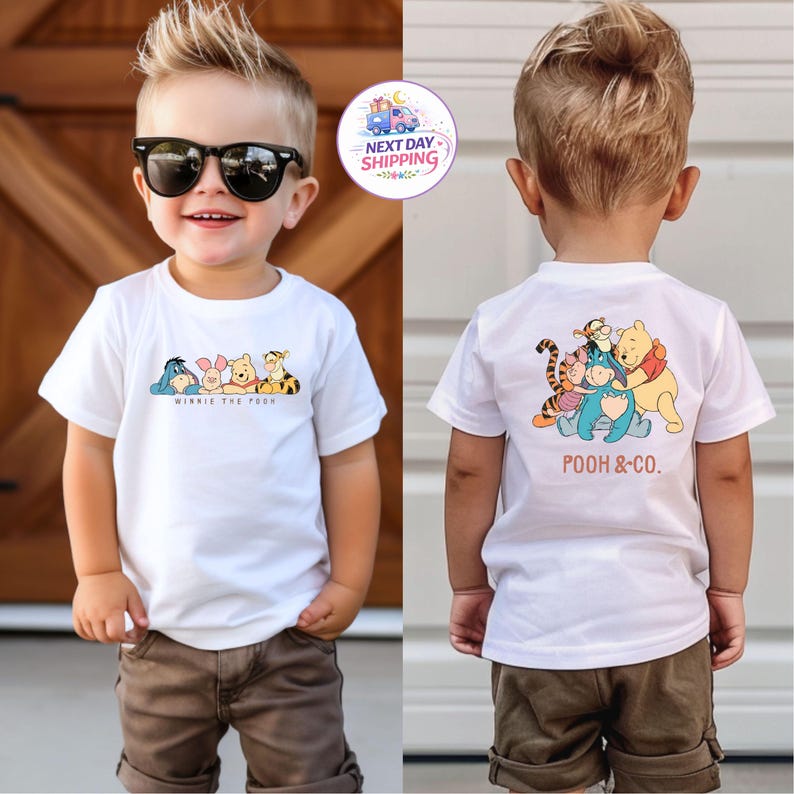 May include: White t-shirt featuring Winnie the Pooh characters on the front and back. The front of the shirt displays Eeyore, Piglet, Winnie the Pooh, and Tigger with the text "Winnie the Pooh". The back shows the characters with the text "Pooh & Co."