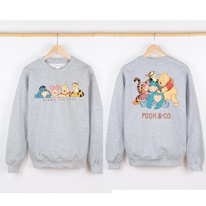 May include: A heather gray sweatshirt featuring the characters from Winnie the Pooh. The front of the sweatshirt displays Eeyore, Piglet, Winnie the Pooh, and Tigger with the text "Winnie the Pooh". The back shows the characters with the text "Pooh & Co."