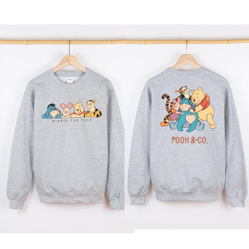 May include: A heather gray sweatshirt featuring the characters from Winnie the Pooh. The front of the sweatshirt displays Eeyore, Piglet, Winnie the Pooh, and Tigger with the text "Winnie the Pooh". The back shows the characters with the text "Pooh & Co."