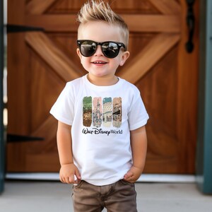 Puede incluir: Camiseta blanca con un gr&aacute;fico colorido con im&aacute;genes de Walt Disney World. La camiseta tiene las palabras "Walt Disney World" impresas en negro. El ni&ntilde;o lleva gafas de sol y pantalones marrones.