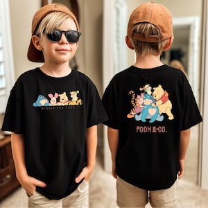 May include: Black t-shirt featuring Winnie the Pooh characters on the front and back. The front displays Eeyore, Piglet, Winnie the Pooh, and Tigger with the text "WINNIE THE POOH". The back shows the characters with the text "POOH & CO."