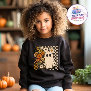 May include: A black long-sleeve sweatshirt featuring a central graphic print of a white ghost surrounded by orange, yellow, and white flowers, set against a black and white checkered background pattern on the front of the garment.