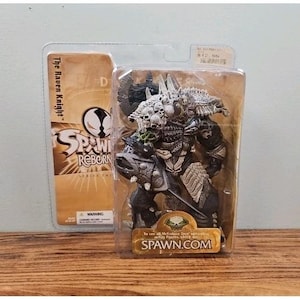 May include: A Spawn Reborn Series Two The Raven Knight action figure in original plastic packaging. The figure features a dark, armored character with skull details and a large axe. The packaging includes the text Spawn Reborn and Spawn.com.