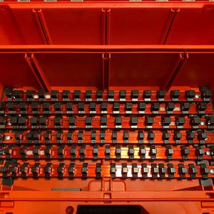 以下が含まれることがあります： 複数のコンパートメントを備えた、開いたオレンジ色のツールボックス。内部には、黒いソケットホルダーの列がオレンジ色のレールに配置されています。ツールボックスは、ツールを整理して保管するように設計されています。