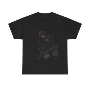 May include: Black t-shirt featuring a seated figure looking at a phone. The illustration depicts a person with dark skin and curly hair, wearing a dark outfit. The artwork is set against a dark background.