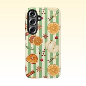 Könnte beinhalten: Eine Handyhülle mit grün-weiß gestreiftem Hintergrund, verziert mit Aquarellillustrationen von Orangenscheiben, Zimtstangen, Sternanis, Äpfeln und Beeren. Die Hülle hat eine Kamera mit drei Objektiven.