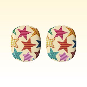 Puede incluir: Dos pendientes ovalados con fondo crema. Cada pendiente presenta un patrón de estrellas coloridas en varios diseños, incluyendo rayas y cuadros. Las estrellas son en tonos rojo, rosa, amarillo, verde y morado.