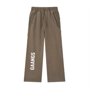 May include: Olive green wide-leg sweatpants with a drawstring waist and side pockets. The word "GAANGS" is printed vertically in white on the left leg. The pants are made of a soft, comfortable material.