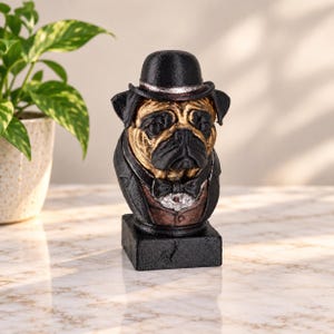 May include: A decorative figurine of a pug dog wearing a black bowler hat, a black tuxedo jacket, and a bow tie. The pug has a tan face with black features, and the entire bust is mounted on a solid black rectangular base with a textured finish.