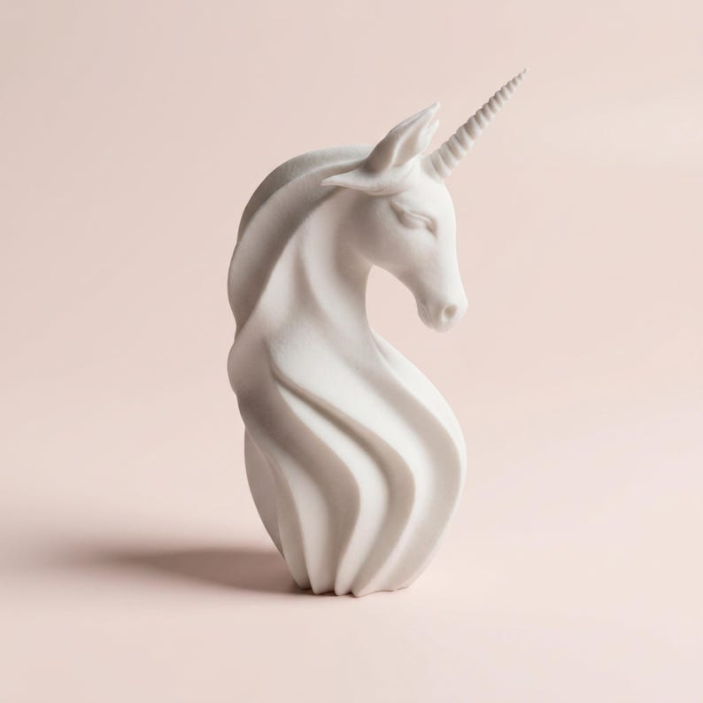 May include: A white unicorn sculpture with a spiraling mane and a detailed horn. The sculpture has a smooth finish and is set against a soft pink background. The unicorn's head is gracefully lowered.