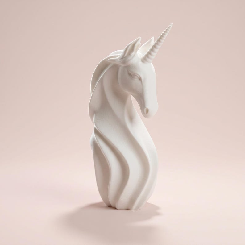 May include: A white unicorn figurine with a spiraling body and a detailed horn. The sculpture has a smooth finish and is set against a soft pink background. The unicorn's head is gracefully tilted.