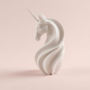 May include: A white unicorn sculpture with a spiraling mane and a detailed, textured horn. The sculpture is set against a soft pink background, highlighting its elegant form and design. The unicorn's head is gracefully curved.