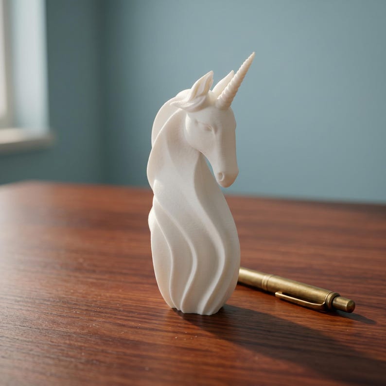 May include: A white unicorn figurine with a spiraling mane and a detailed horn. The sculpture is on a wooden surface, next to a gold-colored pen. The background is a solid blue wall.