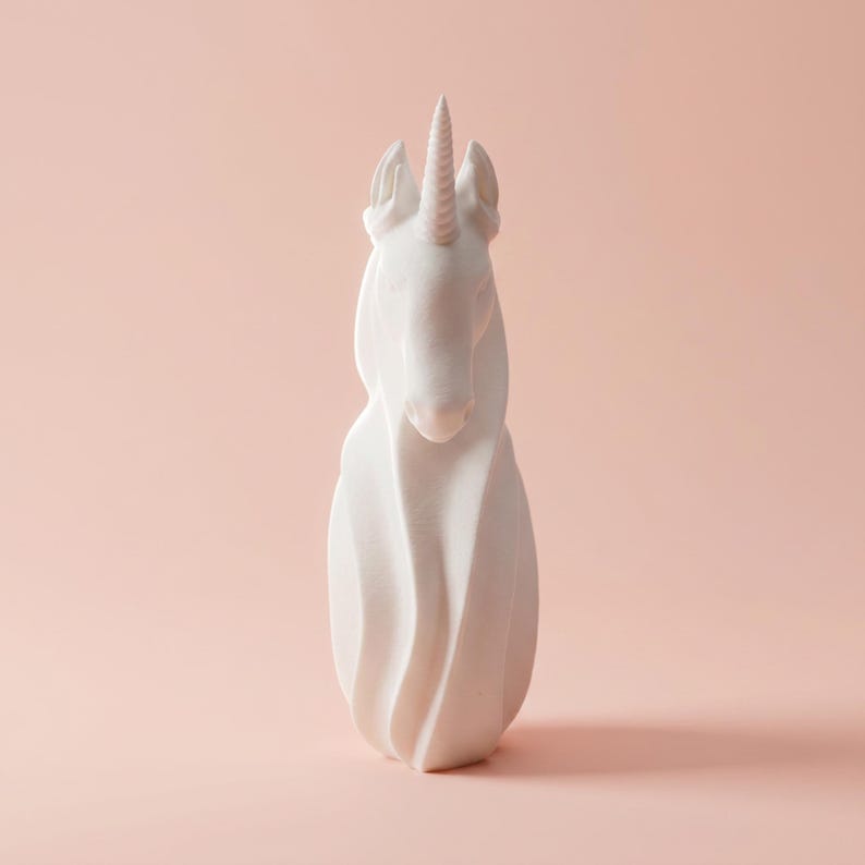 May include: A white unicorn sculpture with a spiraling body and a detailed horn. The sculpture is set against a soft pink background, highlighting its elegant form. This decorative piece is ideal for home decor.