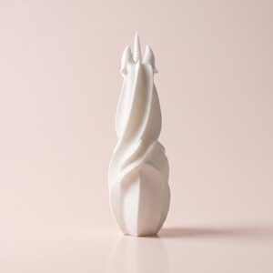 May include: A white, abstract unicorn sculpture with a spiraling body and a single horn. The sculpture has a smooth, matte finish and is set against a soft pink background. The design is modern and minimalist, suitable for home decor.