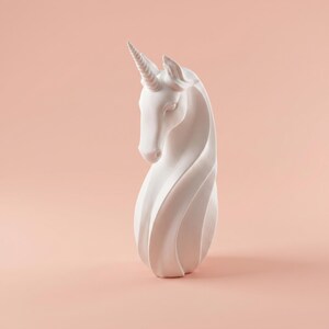 May include: A white unicorn sculpture with a spiraling body and a detailed horn. The sculpture is set against a soft peach background, highlighting its elegant form and design. The unicorn's head is gracefully lowered.
