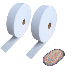 Könnte beinhalten: Zwei große weiße Klebebandrollen mit strukturierter Oberfläche und einem zentralen Pappkern, begleitet von einem kleinen ovalen Teppich mit einem mehrfarbigen konzentrischen Muster in den Farben Rosa, Orange, Gelb, Grün und Blau.