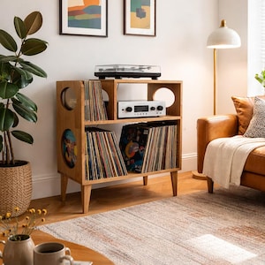 May include: A wooden record storage unit with a turntable on top, filled with vinyl records. The unit has circular cutouts and is set in a living room with art prints, a floor lamp, and a rug.