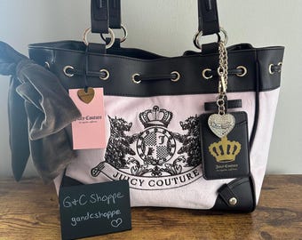 Può includere: Borsa tote Juicy Couture rosa e nera con chiusura a coulisse. La borsa presenta un design a stemma con le parole "Juicy Couture" e un ciondolo a forma di cuore. La borsa ha manici e finiture neri.