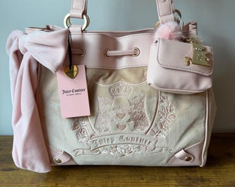 Può includere: Borsa Juicy Couture rosa chiaro con un piccolo portafoglio abbinato. La borsa presenta una chiusura con coulisse, finiture color oro e un grande fiocco. La parte anteriore della borsa presenta un design con stemma ricamato e un'etichetta rosa con il nome del marchio.