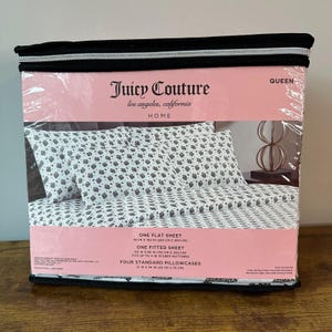 Puede incluir: Un juego de sábanas Juicy Couture Queen empaquetado. El juego incluye una sábana encimera (229 cm x 259 cm), una sábana bajera (152 cm x 203 cm) y cuatro fundas de almohada estándar (53 cm x 76 cm). Las sábanas tienen un fondo blanco con un estampado gris.