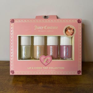 Puede incluir: Un set Juicy Couture Lip & Cheek Tint Collection en una caja rectangular rosa que contiene cuatro frascos de vidrio con tapas blancas. Los tintes son de tonos beige claro, bronceado, rosa polvoriento y malva. La caja indica 40 ml en total.