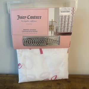 May include: A Juicy Couture printed shower curtain with hooks. The curtain is white with pink text and bow patterns. The packaging includes a set of silver-coloured shower curtain hooks. The curtain measures 178 cm x 183 cm.