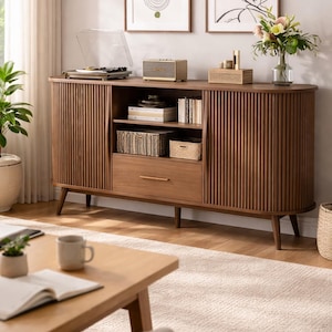 May include: A mid-century modern style wooden media console with a fluted front. The console features a drawer, open shelving, and a turntable. A small speaker and decorative items sit on top. Two framed art prints hang on the wall above.