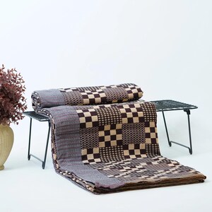 May include: A folded textile featuring a patchwork design with alternating squares of dark brown and beige checkerboard patterns alongside sections of intricate, fine-textured geometric weaves in shades of brown, beige, and dark gray.