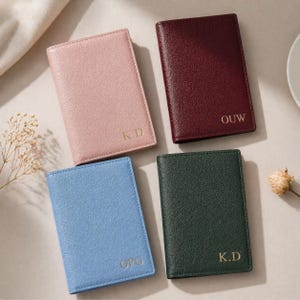 Puede incluir: Cuatro fundas rectangulares para pasaporte en rosa claro, rojo oscuro, azul claro y verde oscuro. Cada funda tiene una superficie texturizada e iniciales doradas en relieve: K.D en la rosa, OUW en la roja, OPG en la azul y K.D en la verde.