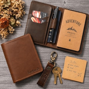 Puede incluir: Un conjunto de accesorios de viaje de cuero marrón, que incluyen un tarjetero, una cartera, un cuaderno y un llavero. El cuaderno dice "ADVENTURE AWAITS". También hay una lista de tareas pendientes.
