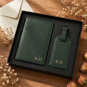 Puede incluir: Un portapasaporte y una etiqueta de equipaje a juego en color verde oscuro, ambos con acabado texturizado y las iniciales K.D. grabadas en oro. Los artículos se presentan en una caja de regalo negra con compartimentos a medida para cada pieza.